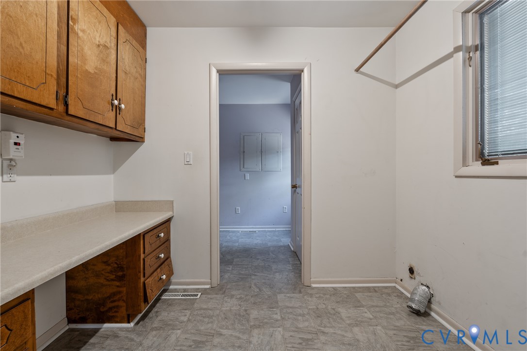 Utility area featuring wood cabinetry, laminate countertops with an integrated workspace, tile flooring, and a wall-mounted hanging rod