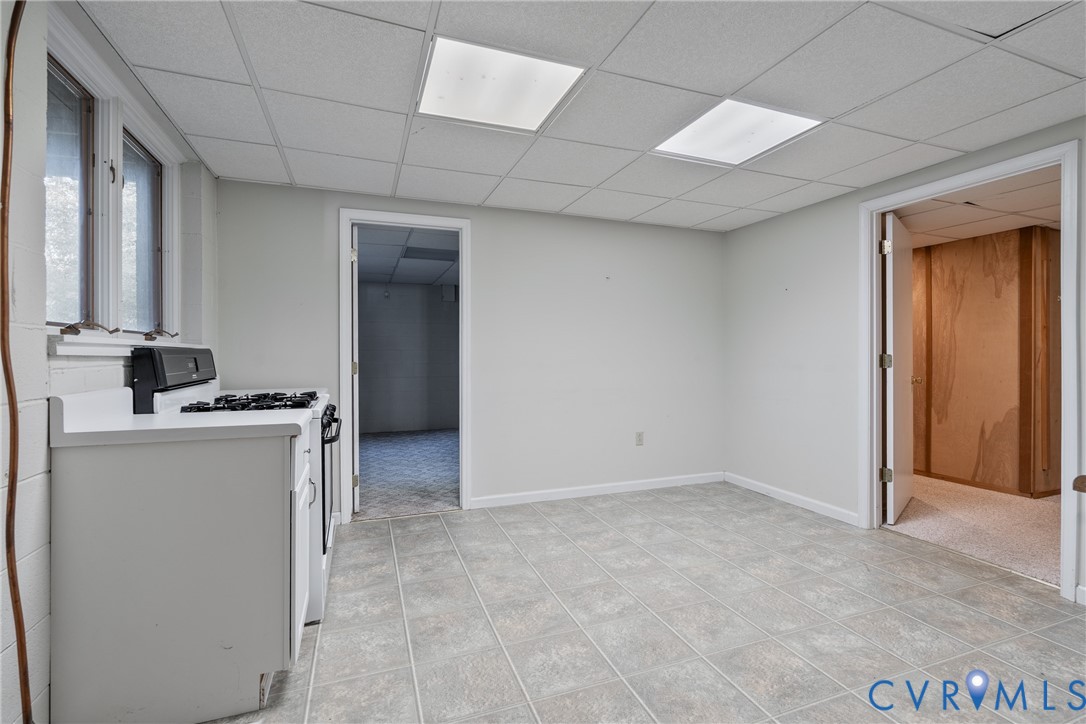 Interior space featuring a suspended drop ceiling with recessed panel lighting, tiled flooring, painted concrete block walls, and a built-in range