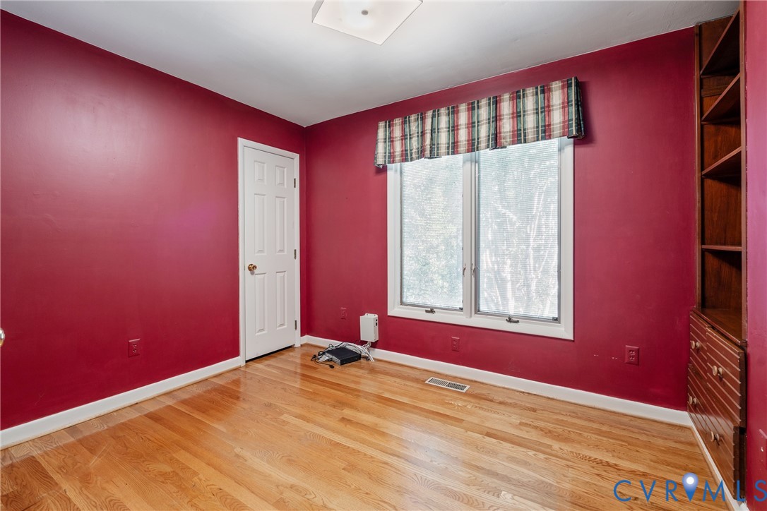 Room featuring wood-finish flooring, built-in wooden shelving, and a double-pane window