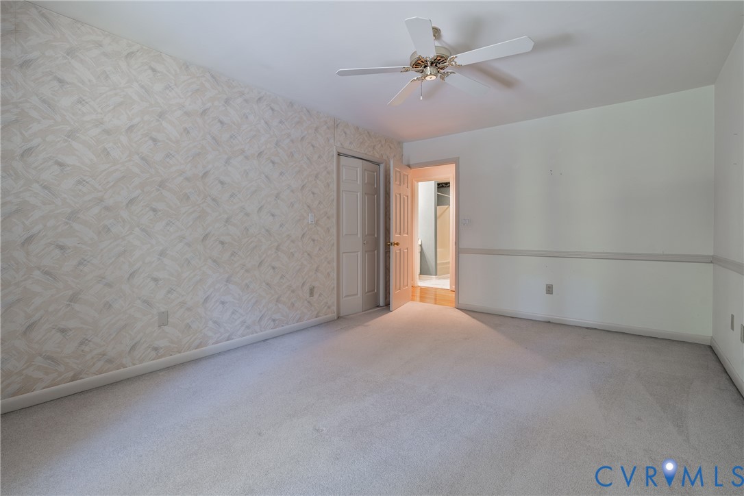 Room featuring textured wallpaper, neutral carpeting, a ceiling-mounted fan, and double-panel closet doors