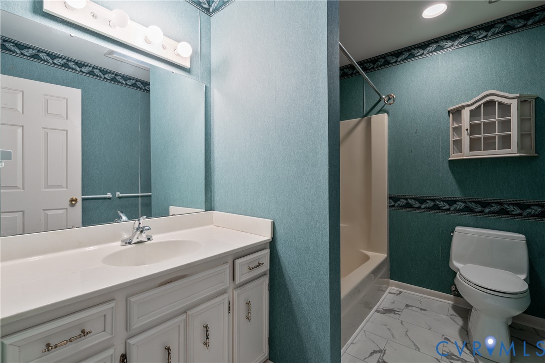 Bathroom featuring a vanity with white cabinetry and a solid-surface countertop, an integrated sink with a chrome faucet, a wall-mounted medicine cabinet, and stone-finish tile flooring