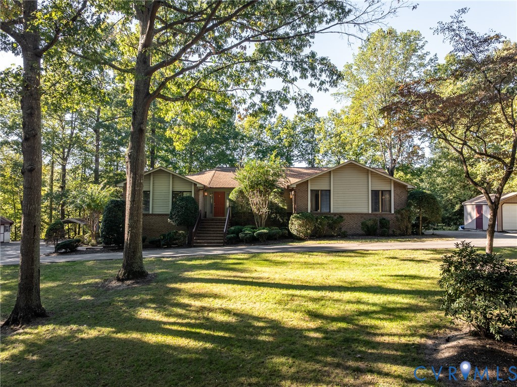 Exterior featuring a brick and siding facade, covered front entry with stairs, expansive lawn, mature trees, and a detached garage