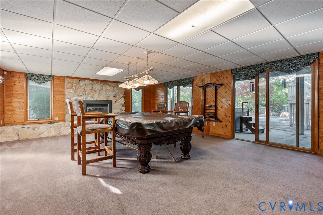 Stone masonry fireplace, wood-paneled walls, sliding glass door, recessed lighting, and wall-mounted shelving unit