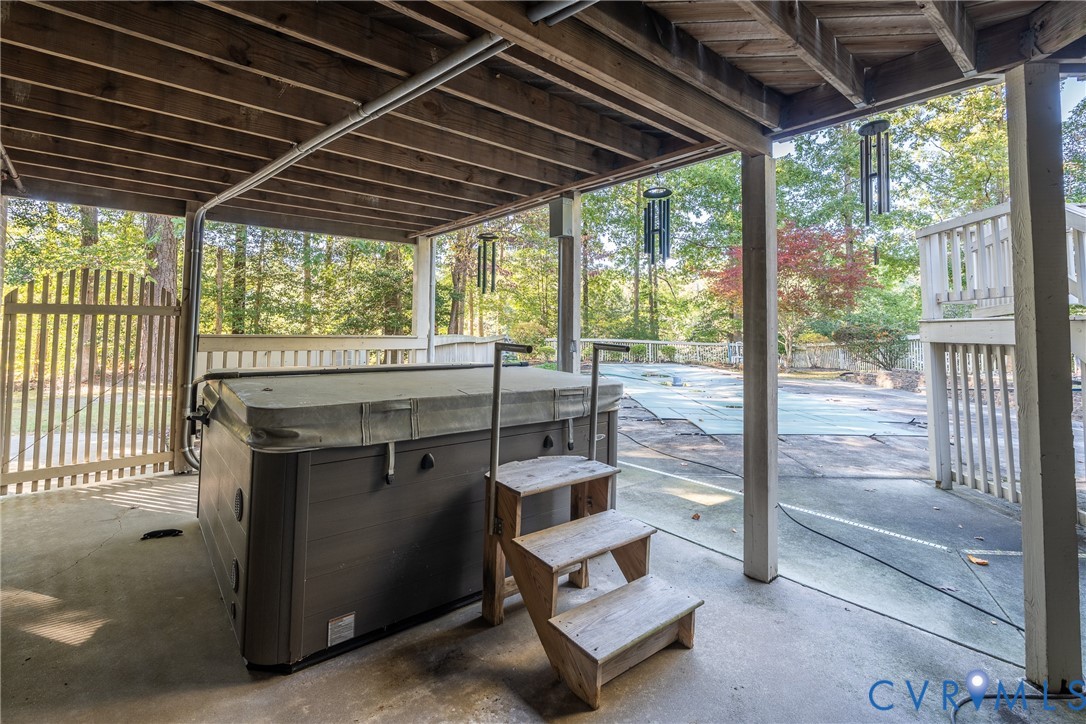 Covered concrete patio featuring a built-in hot tub with stairs, vertical wood-slat fencing, and a fenced swimming pool area