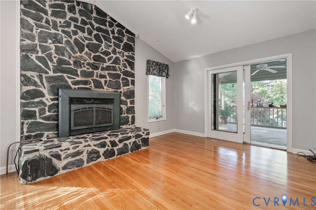Floor-to-ceiling stone fireplace, wood-finish flooring, vaulted ceiling, and sliding glass doors with access to an exterior deck
