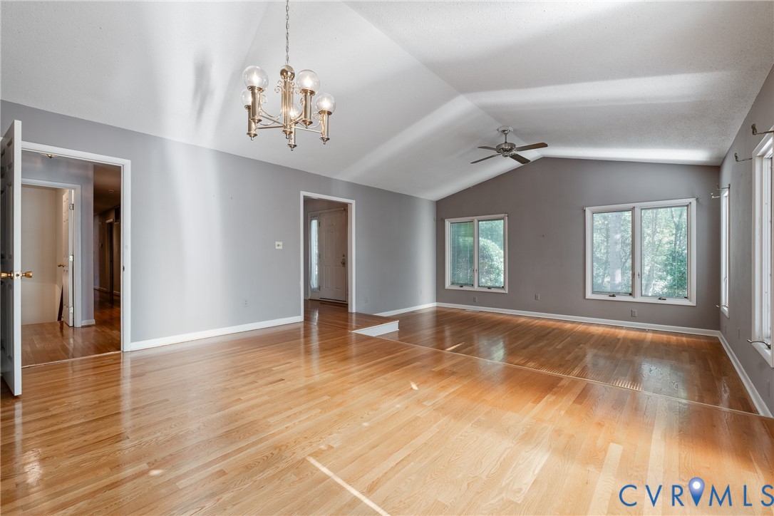 Vaulted ceilings with a five-light chandelier, wood-finish flooring, and multiple dual-pane windows