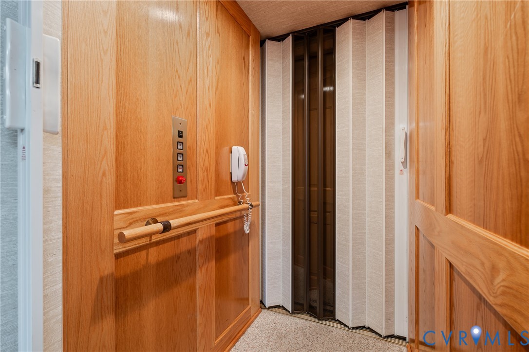 Interior elevator featuring wood paneling, a mounted control panel, a horizontal wooden grab bar, and a bi-fold folding door