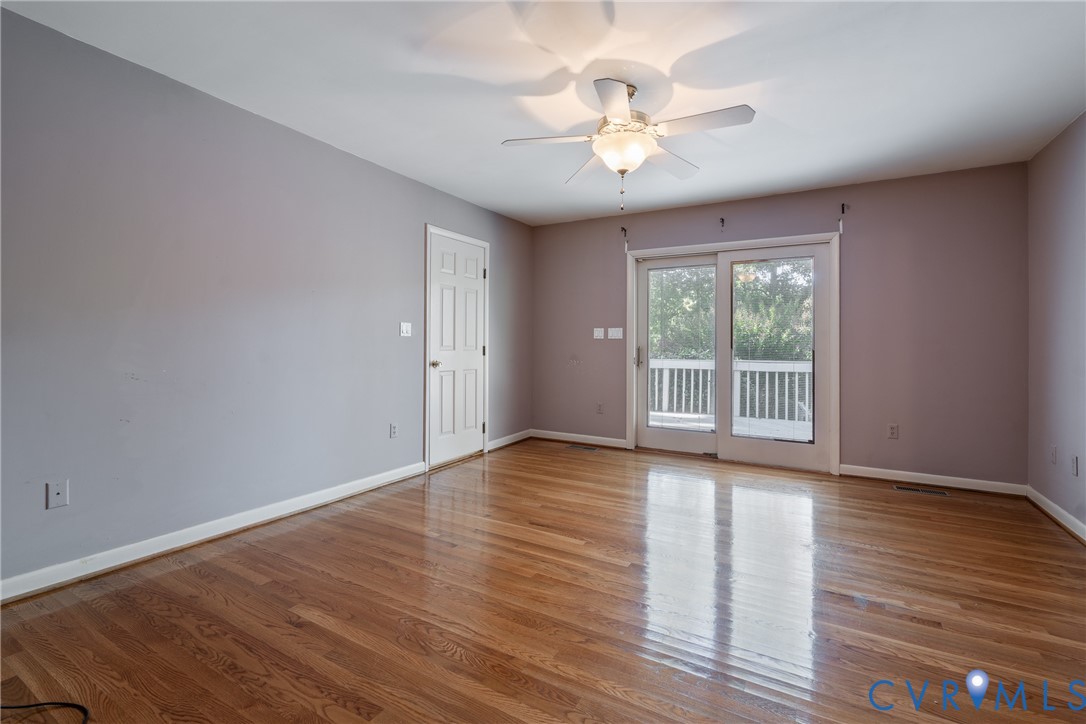 Room featuring wood-finish flooring, a ceiling fan with integrated lighting, a six-panel interior door, and sliding glass doors opening to an exterior deck