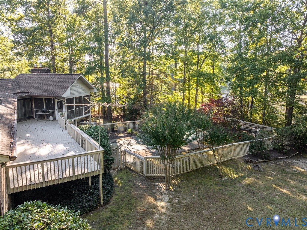 Elevated wooden deck with balustrade railings, screened-in porch, fenced-in pool area, and mature perimeter trees