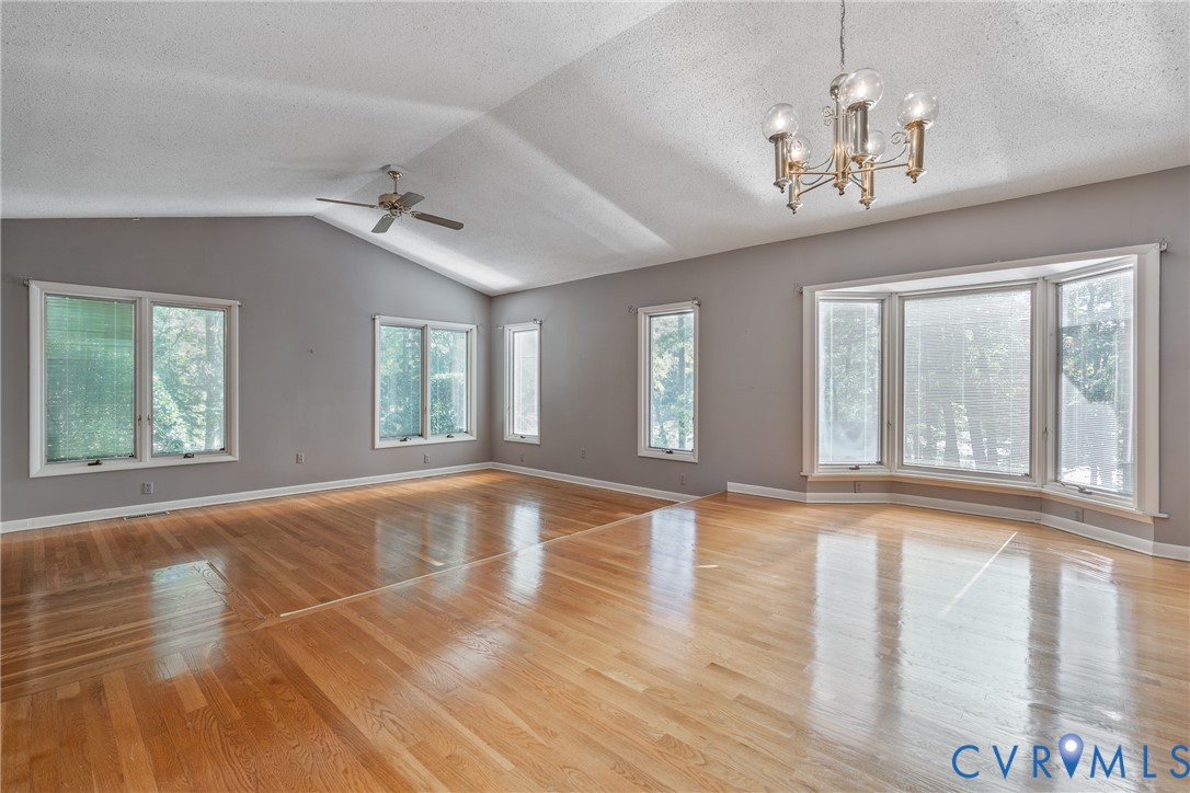 Vaulted ceilings, wood-finish flooring, multi-pane windows, a bay window, and a multi-arm chandelier