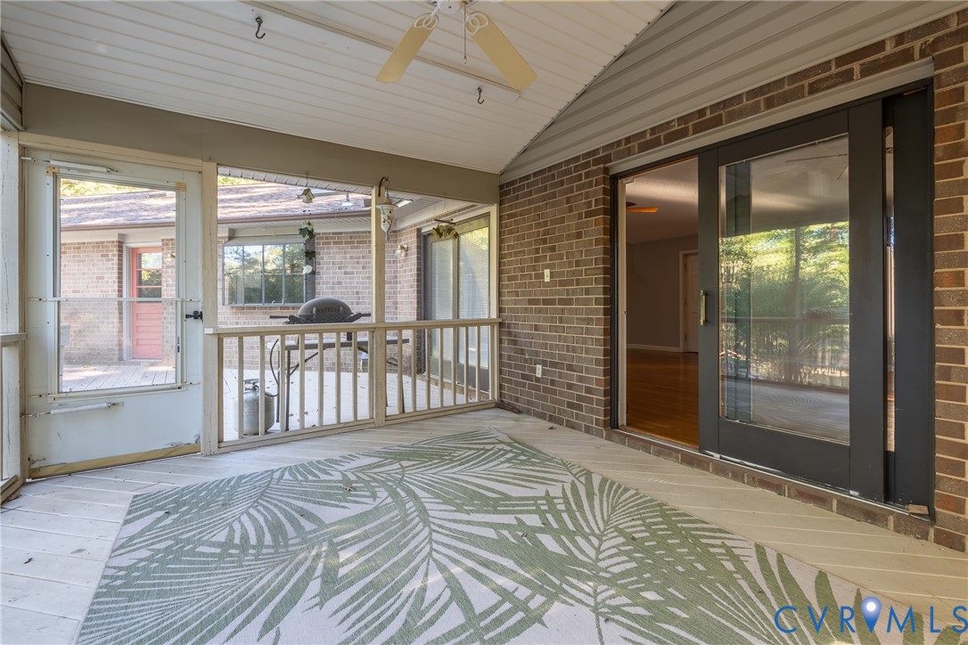 Screened-in porch featuring brick exterior walls, wood-finish flooring, a ceiling fan, and sliding glass entry doors