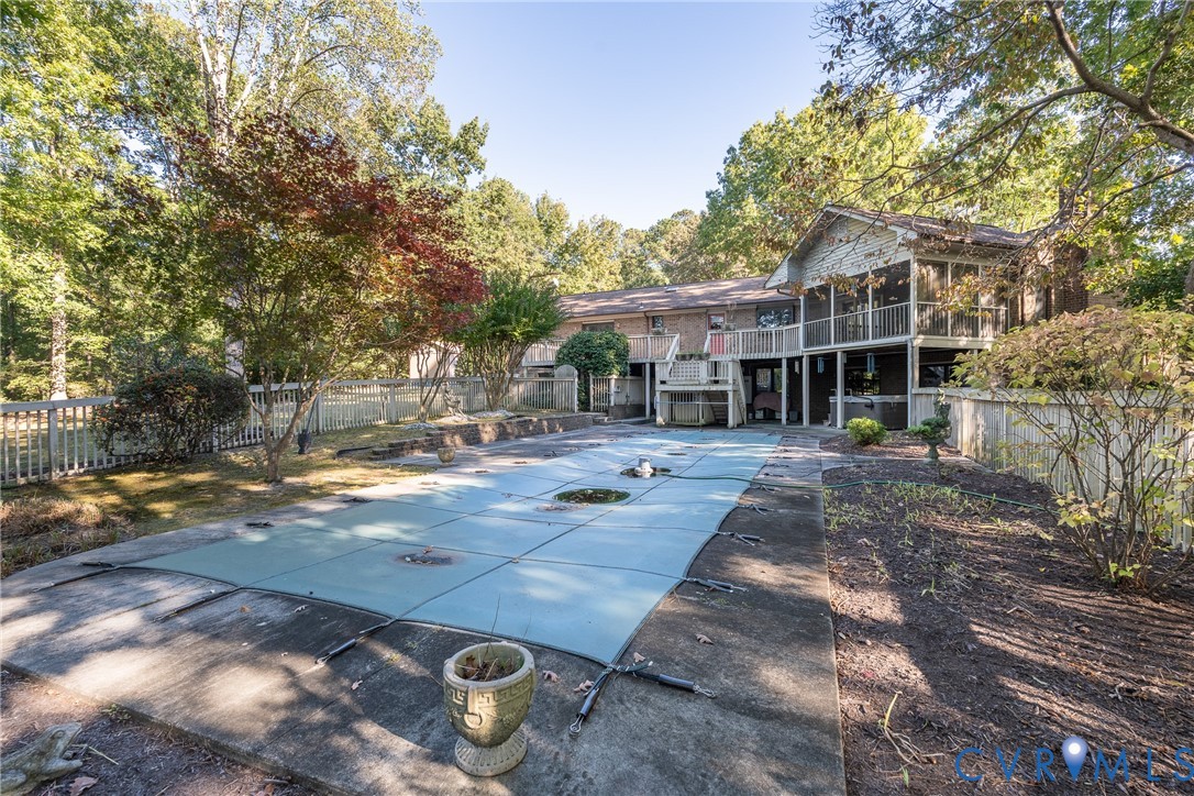 Rear exterior featuring a covered deck, screened porch, swimming pool with safety cover, concrete decking, and perimeter fencing