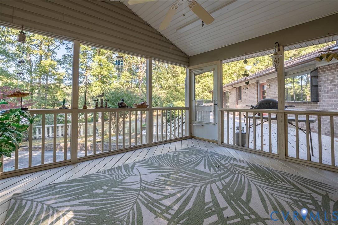 Screened-in porch featuring wood-plank flooring, a vaulted ceiling with a mounted fan, and wooden railings