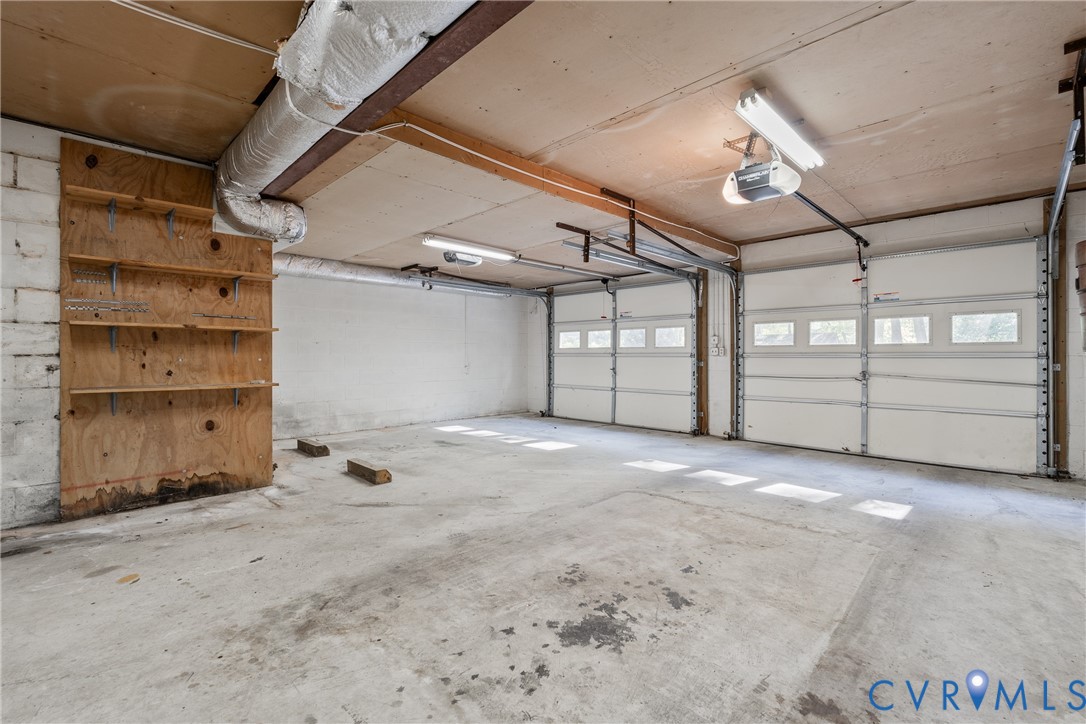 Two-car garage featuring segmented overhead doors with windows, exposed ceiling joists, concrete flooring, and built-in wood shelving