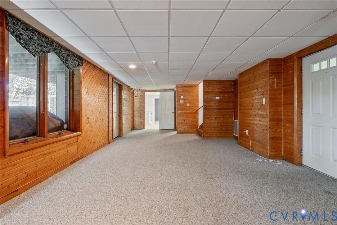 Wood-paneled walls, carpeted flooring, drop ceiling, and multiple white-paneled doors