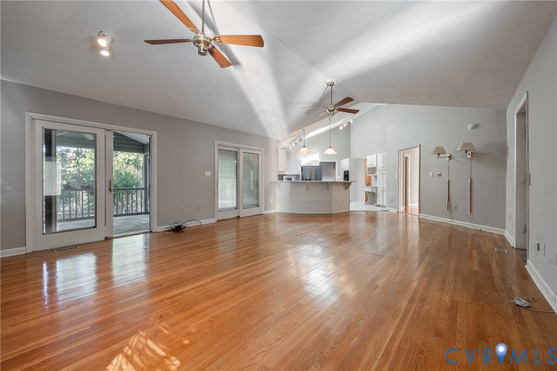 Open-concept interior featuring vaulted ceilings, wood-finish flooring, dual ceiling fans, sliding glass doors, and a built-in kitchen peninsula
