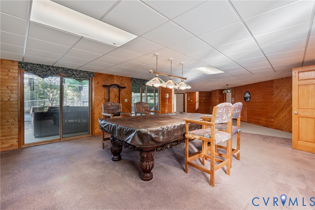 Wood-paneled walls, sliding glass door, multi-light pendant fixture, drop ceiling, and carpeting