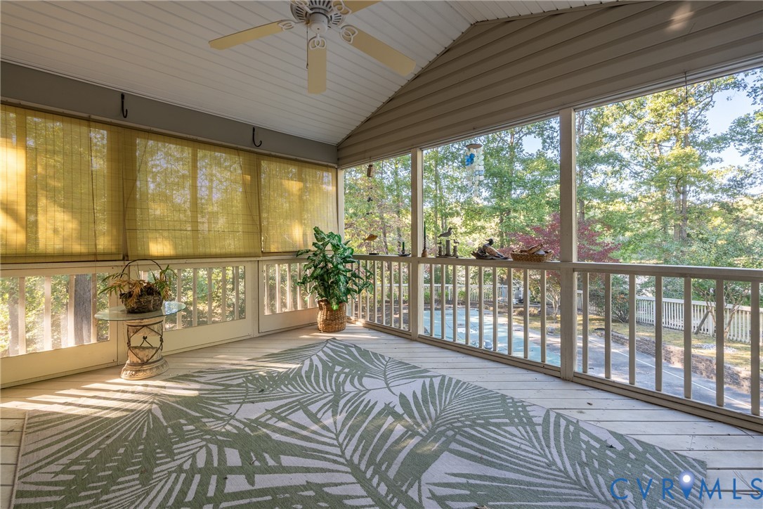 Screened-in porch featuring painted wood decking, a vaulted ceiling, and an integrated ceiling fan