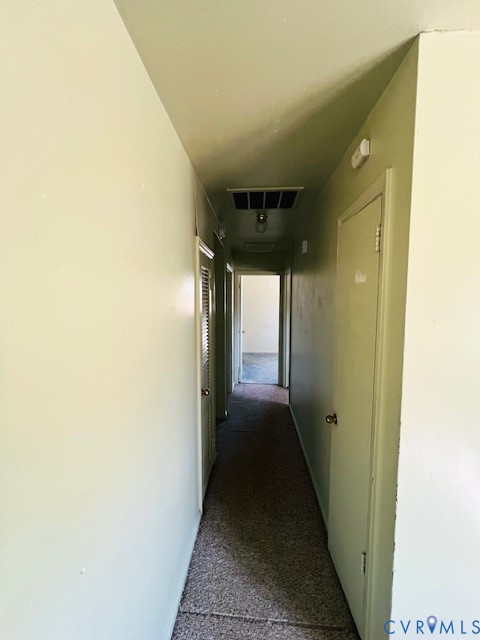 Hallway featuring neutral-toned wall paint, carpeted flooring, multiple interior doors, and overhead lighting