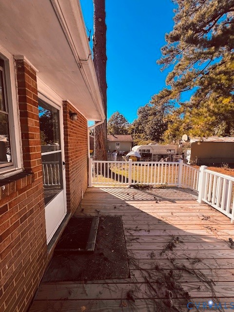 Exterior brick facade featuring a wood-plank deck enclosed by white vinyl railings