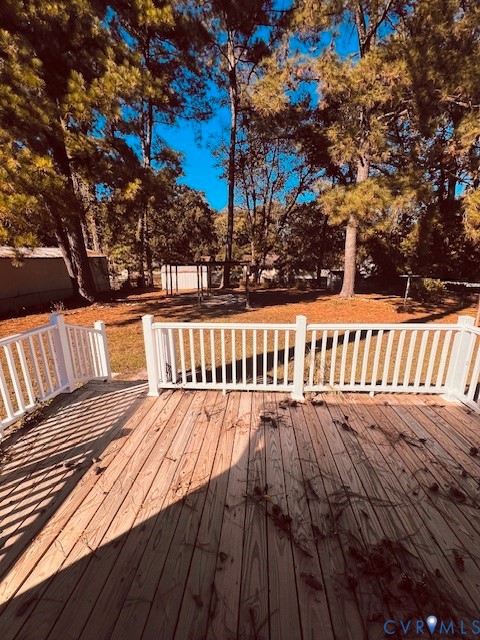 Wood-plank decking featuring white vinyl railing, encompassing a backyard with mature trees and a detached structure
