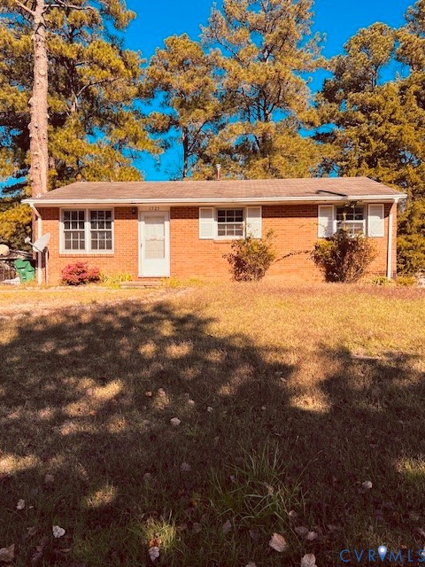 Single-story brick exterior featuring a gable roof, white window shutters, and a wood-surrounded lot with mature trees