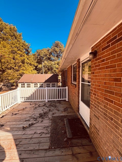 Elevated wood deck featuring white railing and red brick exterior wall with a storm door