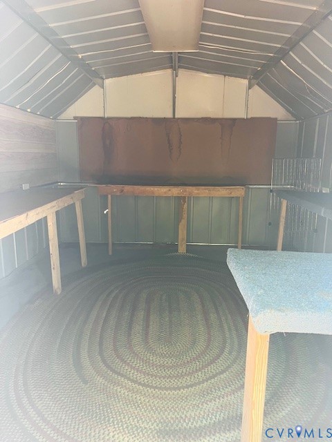 Outbuilding featuring metal wall construction, a pitched roof, built-in wooden workbenches, and overhead lighting