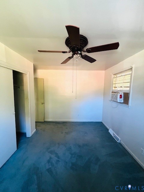 Interior space featuring carpeted flooring, a ceiling fan with integrated lighting, and a window with a mounted cooling unit