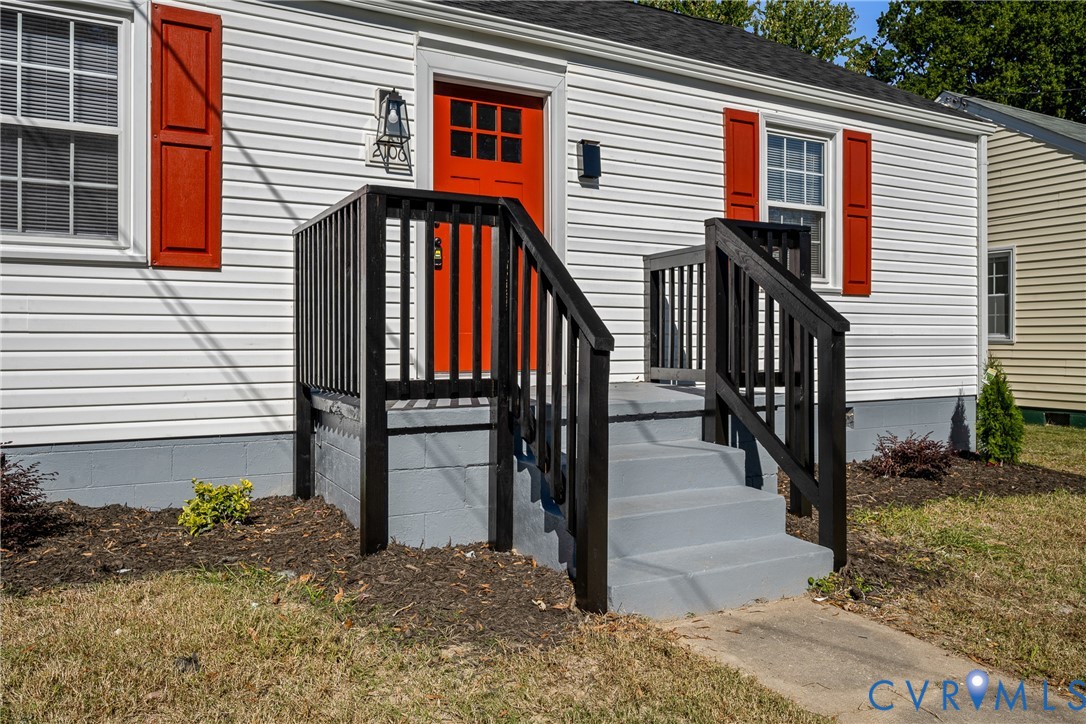 Exterior featuring white horizontal siding, contrasting red shutters, a dedicated front entry with a raised porch, black wooden railing, and a painted concrete staircase Exterior featuring white horizontal siding, contrasting red shutters, a dedicated front entry with a raised porch, black wooden railing, and a painted concrete staircase