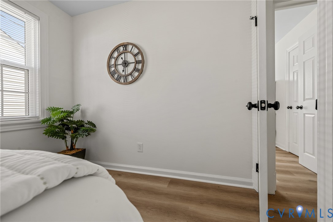 Interior space featuring wood-finish flooring, white walls, and a single-hung window with horizontal blinds