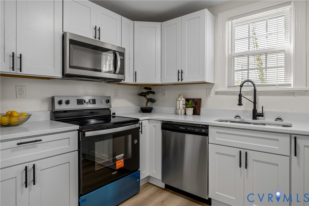 Kitchen featuring white shaker-style cabinetry, stainless steel appliances, white solid-surface countertops, and a matte black gooseneck faucet Kitchen featuring white shaker-style cabinetry, stainless steel appliances, white solid-surface countertops, and a matte black gooseneck faucet