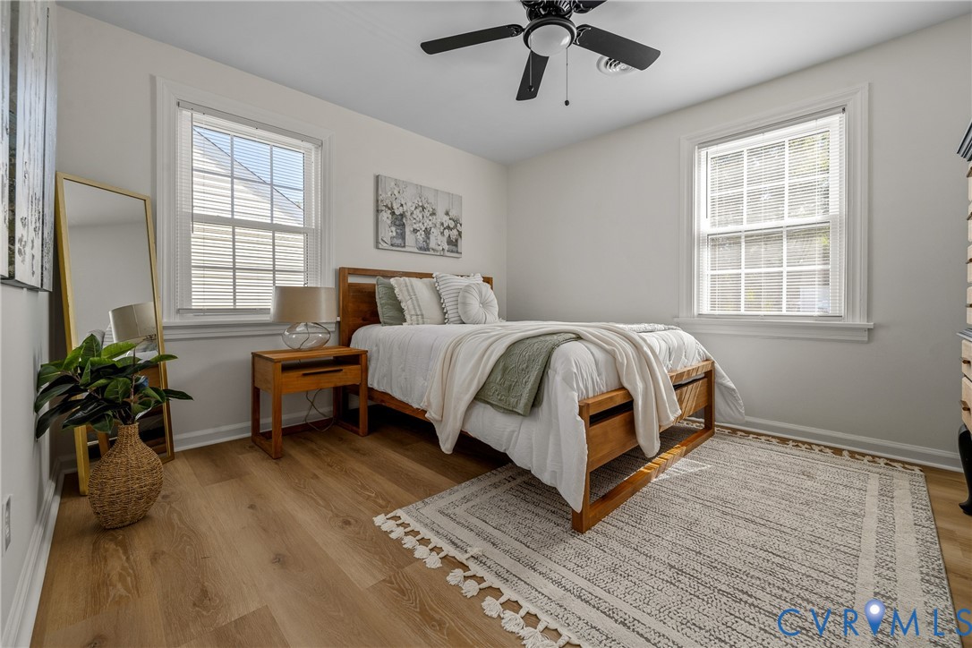 Wood-finish flooring, dual windows with grid detailing, and a ceiling fan with an integrated light fixture
