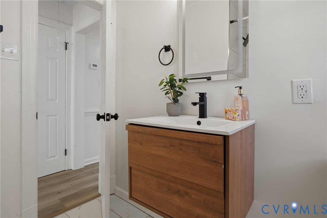 Wall-mounted vanity featuring wood-finish cabinetry, a white integrated rectangular sink, a modern matte black faucet, and a rectangular LED-backlit mirror