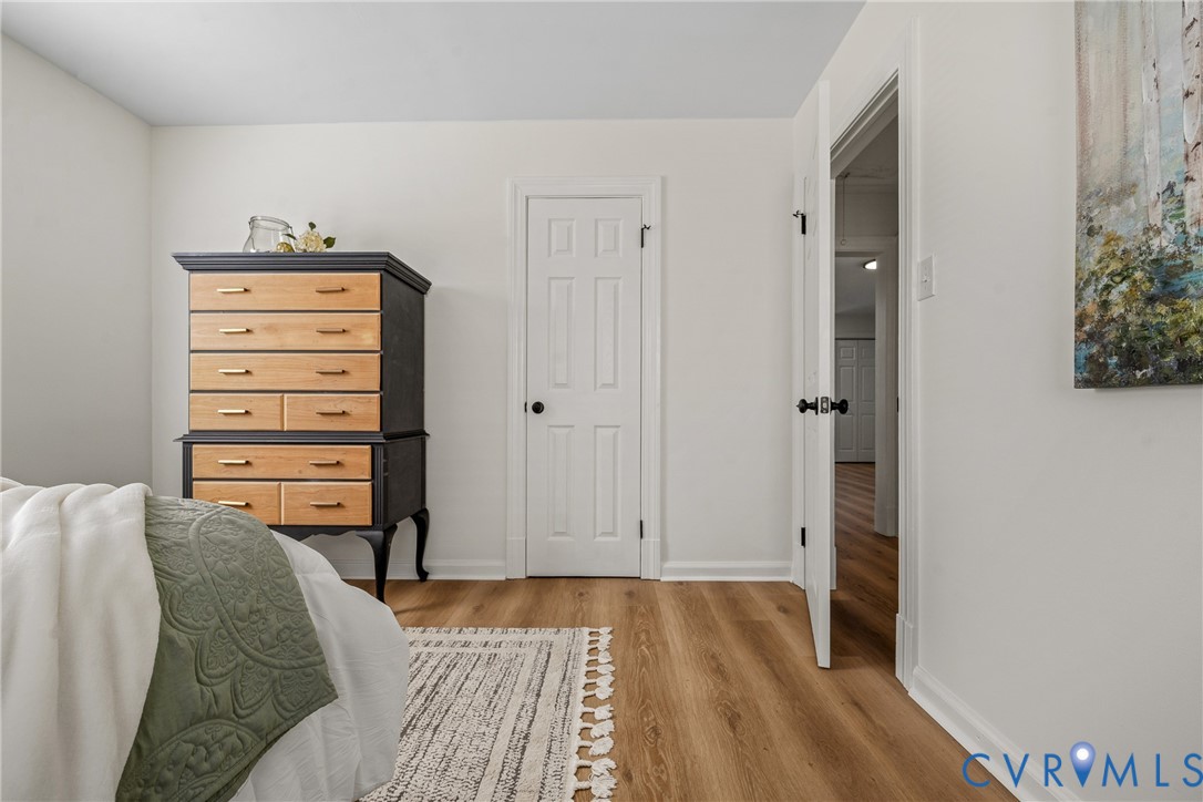Neutral-toned interior room featuring wood-finish flooring, white walls, and a six-panel door with matte black hardware