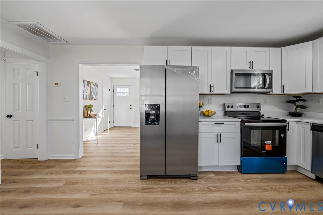 Kitchen featuring white shaker-style cabinetry, wood-finish flooring, stainless steel side-by-side refrigerator, built-in microwave, and electric range
