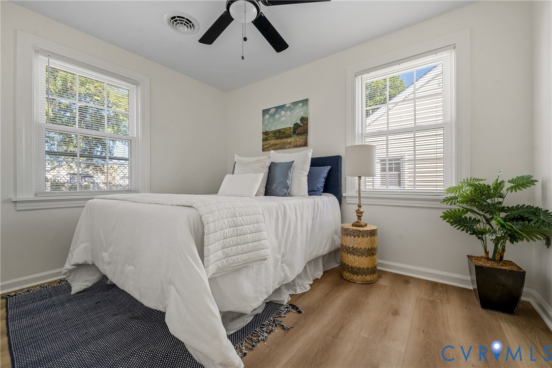 Neutral-toned interior room featuring wood-finish flooring, dual windows with grid detailing, and a ceiling-mounted fan with integrated lighting