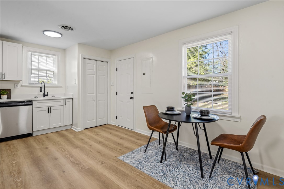 Kitchen featuring white shaker cabinetry, stainless steel dishwasher, matte black faucet, wood-finish flooring, and double-hung windows Kitchen featuring white shaker cabinetry, stainless steel dishwasher, matte black faucet, wood-finish flooring, and double-hung windows