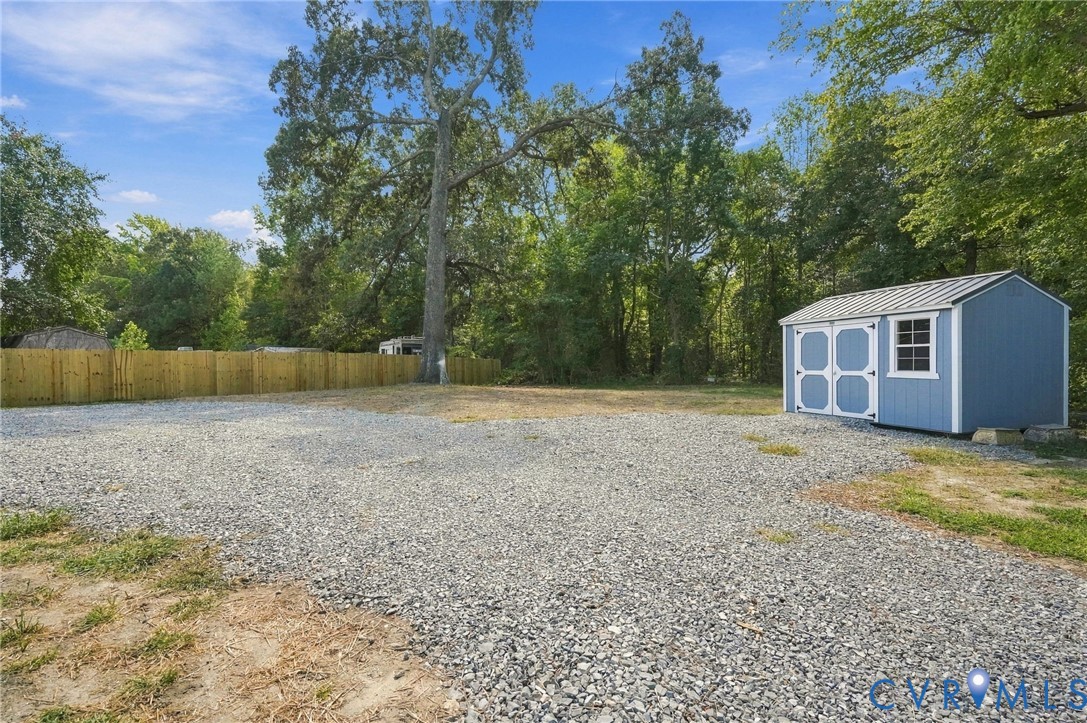 Expansive leveled lot featuring a crushed stone surface, wood-paneled privacy fencing, and a detached storage shed with a metal roof
