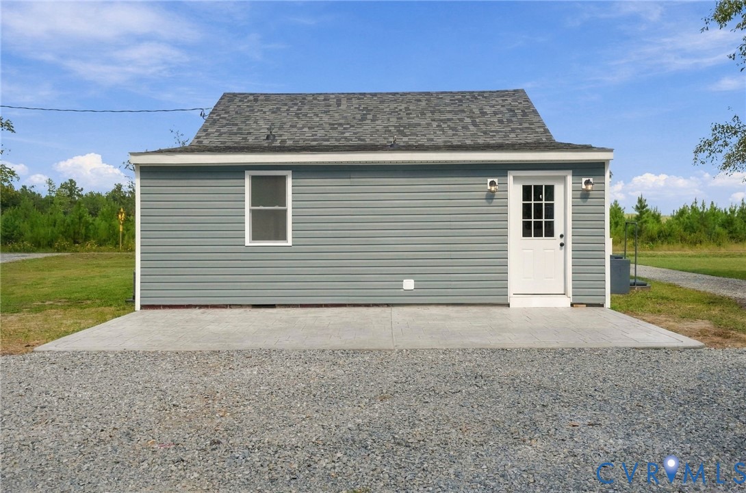 Detached structure featuring blue vinyl siding, a gabled roof with asphalt shingles, a concrete pad entrance, and exterior wall-mounted lighting fixtures