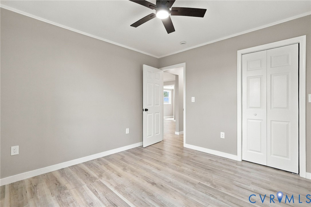 Neutral-toned interior space featuring wood-finish flooring, a ceiling fan with integrated lighting, and a six-panel closet door