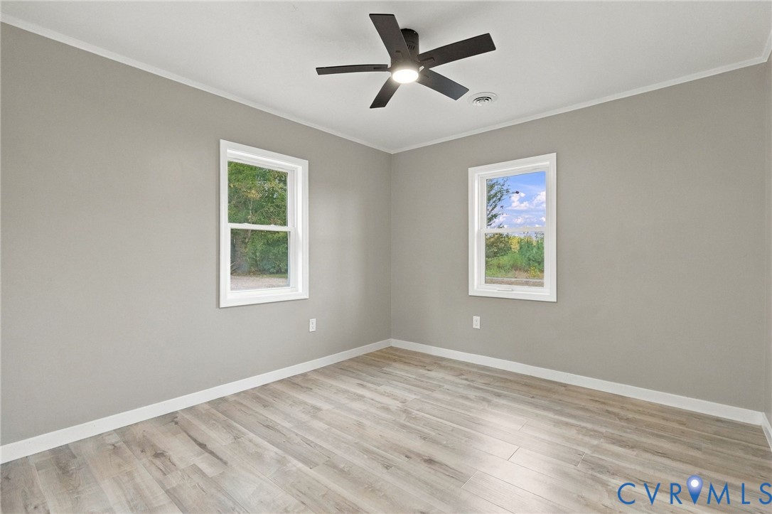 Neutral-toned interior featuring wood-finish flooring, two double-hung windows, and a central ceiling fan with an integrated light fixture