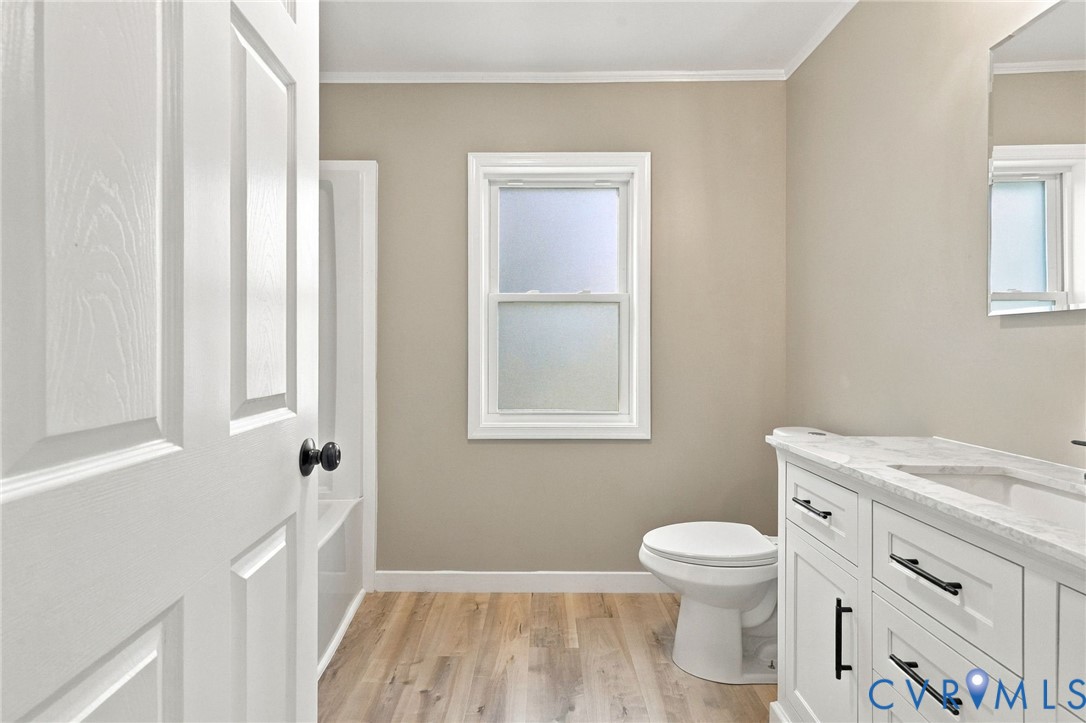 Bathroom featuring wood-finish flooring, a white vanity with stone-style countertop, matte black hardware, and an opaque glass window