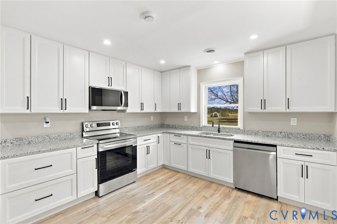 Kitchen featuring shaker-style white cabinetry, stone-finish countertops, stainless steel appliances, recessed lighting, and wood-finish flooring