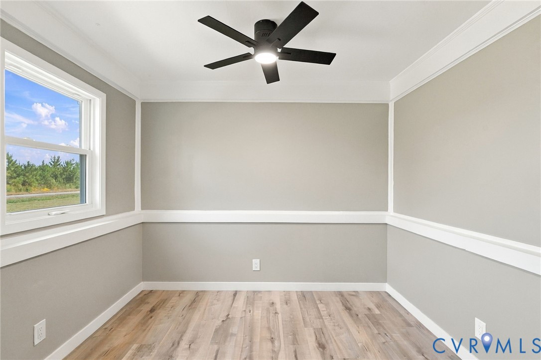 Room featuring wood-finish flooring, white crown molding, chair rail trim, and a ceiling-mounted light fixture Room featuring wood-finish flooring, white crown molding, chair rail trim, and a ceiling-mounted light fixture