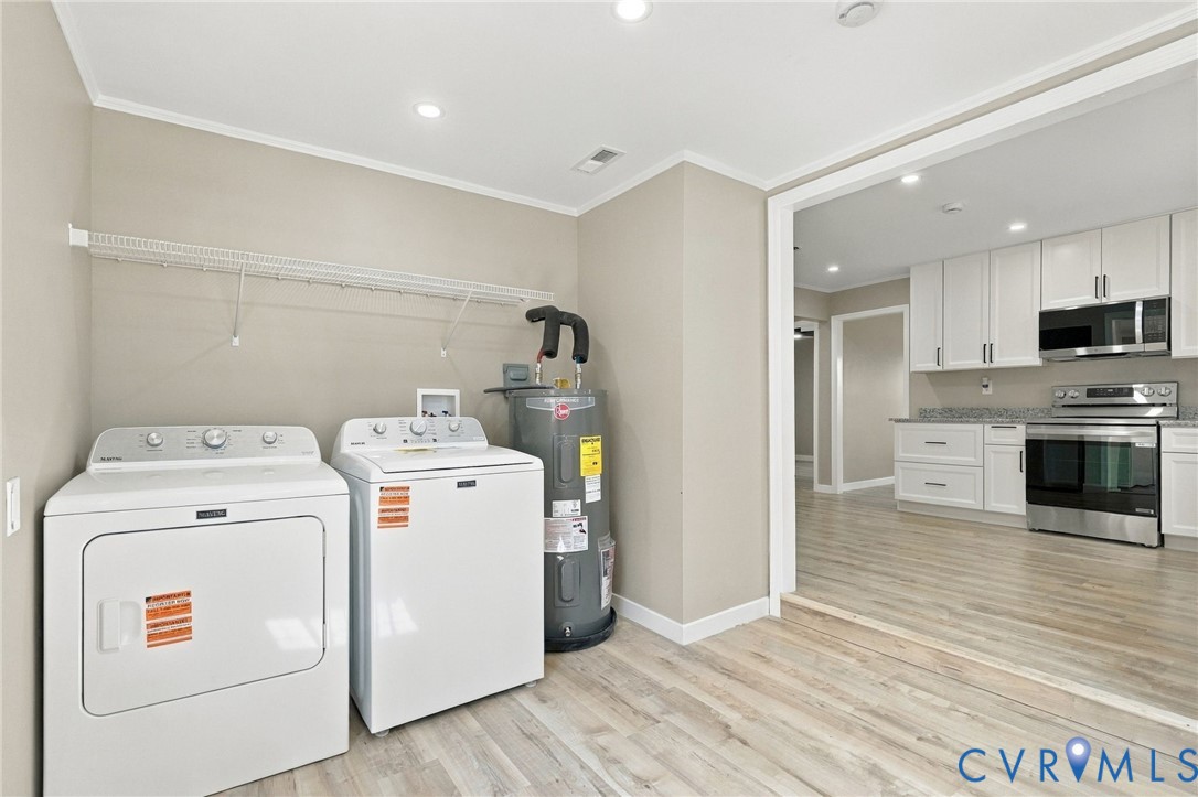 Laundry area featuring wall-mounted wire shelving and wood-finish flooring, opening into a kitchen equipped with white cabinetry, stone-finish countertops, and stainless steel appliances