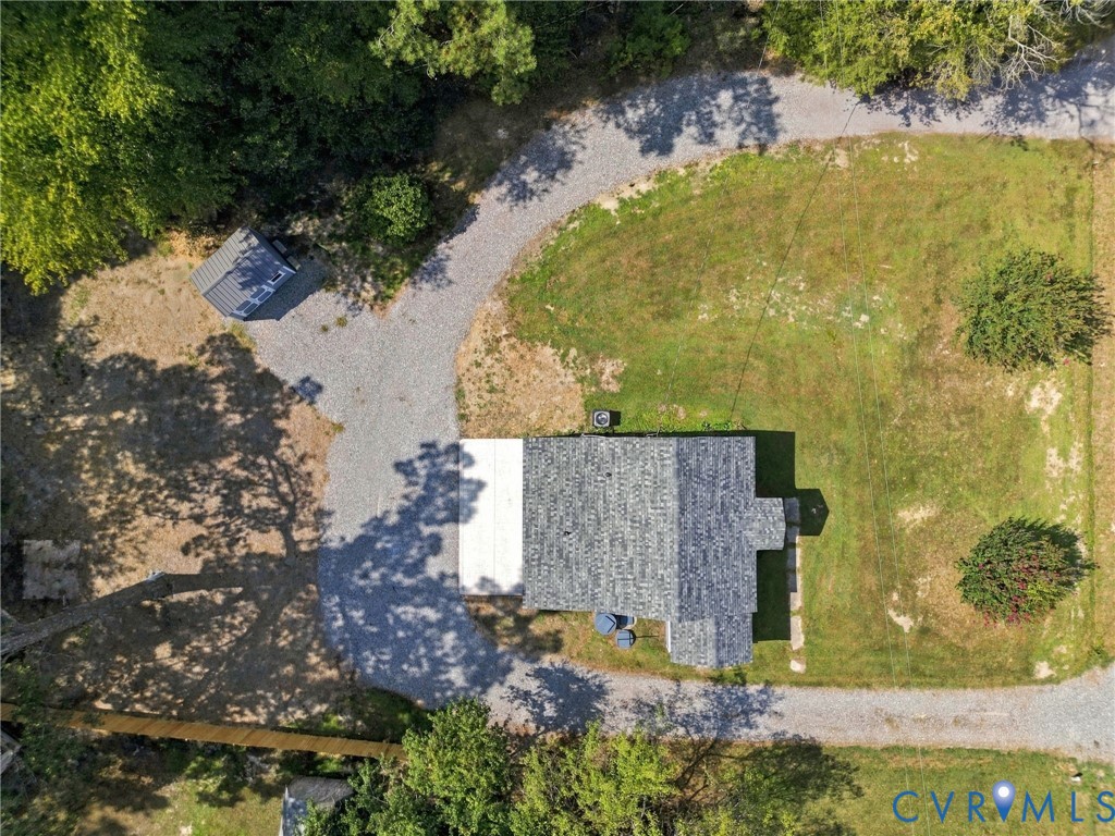 Aerial perspective featuring a gravel driveway, detached storage structure, and expansive grass acreage with mature trees