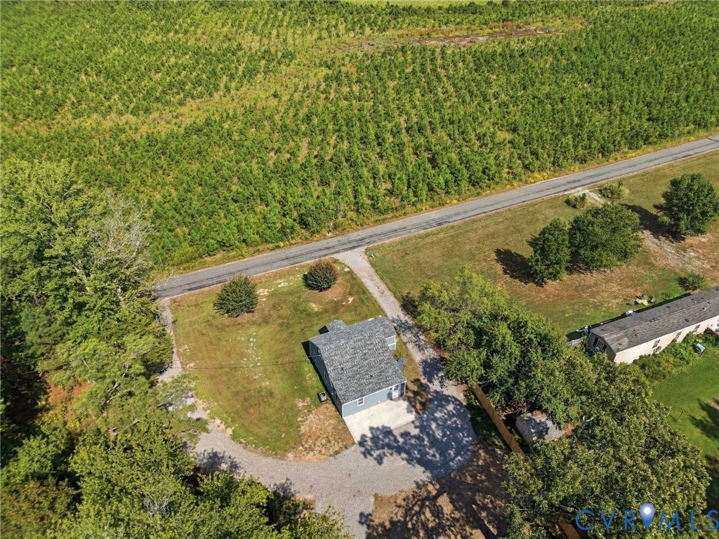 Aerial perspective of a property featuring a detached structure with a pitched roof, gravel driveway, mature trees, and expansive open space