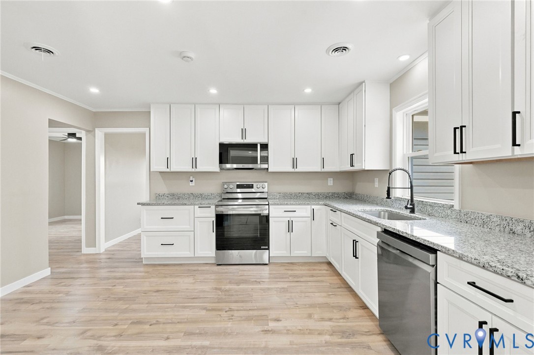 Kitchen featuring white shaker-style cabinetry, stone-finish countertops, stainless steel appliances, matte black hardware, and wood-finish flooring
