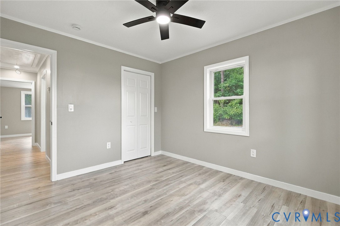Neutral-toned interior space featuring light-colored wood-finish flooring, a ceiling fan with integrated lighting, and a single-panel interior door